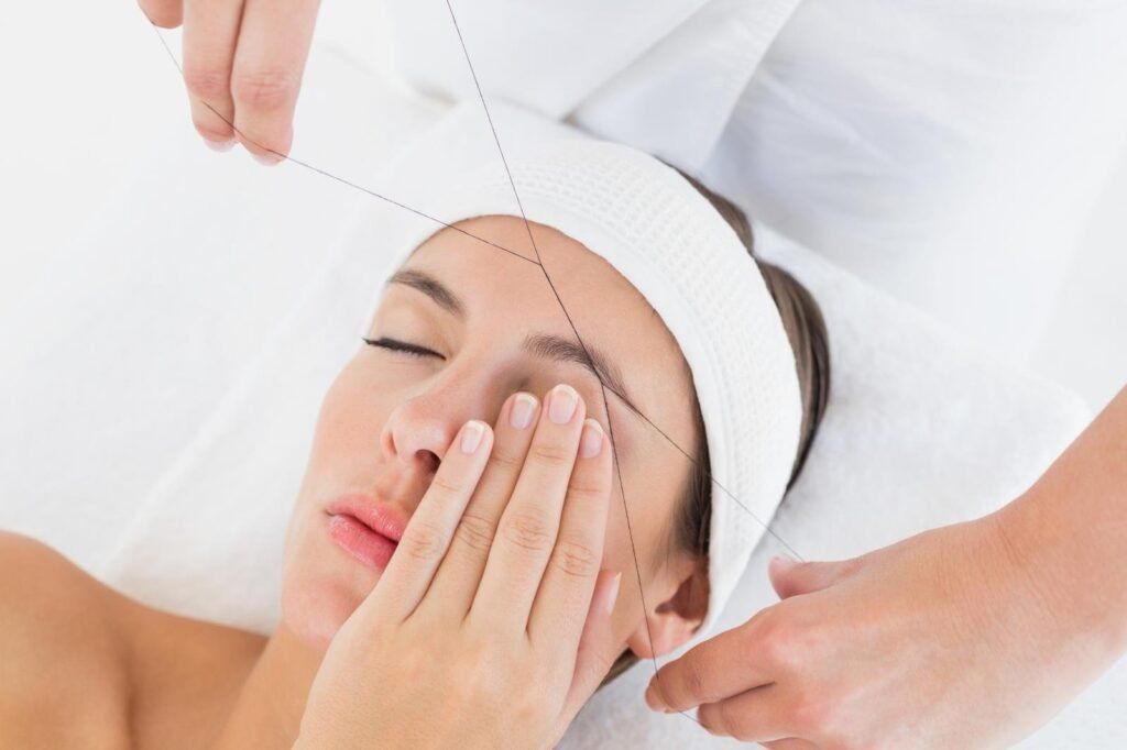 Facial treatment in progress as a client lies with eyes closed while a technician applies a mask with a brush
