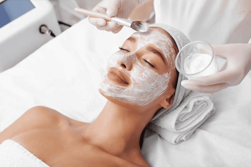 Facial treatment with white cream being applied to a woman’s face in a spa bed