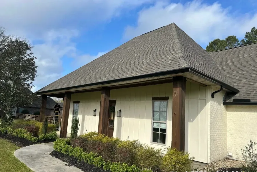 Single-story cream house with gray roof, front porch, and shrubs along a curved walkway