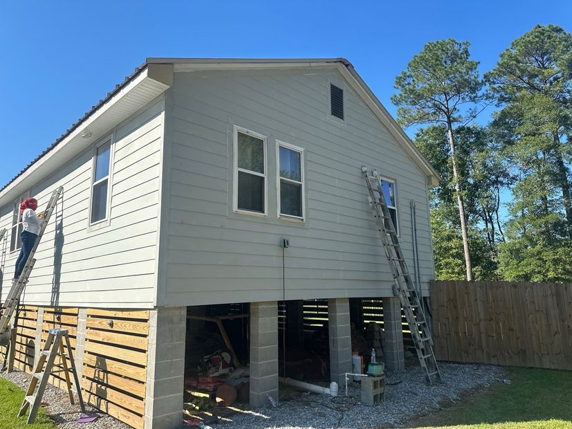 Raised house exterior under renovation with workers on ladders and exposed foundation posts