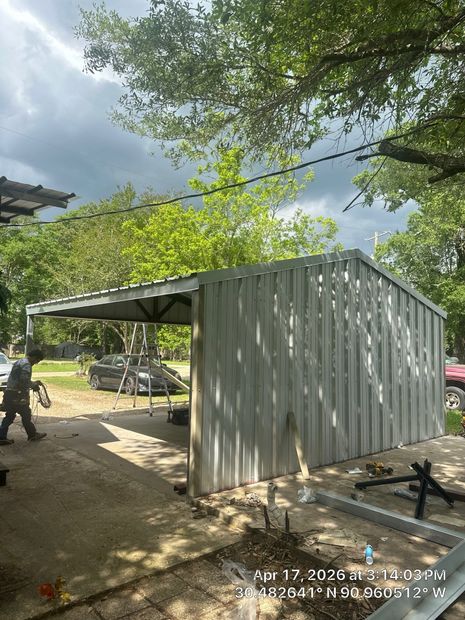 Small corrugated metal shed beside a tree-lined yard, with a person standing nearby and a truck in the background.
