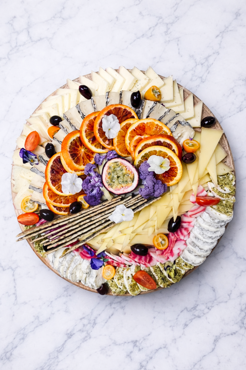 Assortiment de fruits et de fromages tranchés disposés sur un plat rond avec des crackers sur une surface en marbre