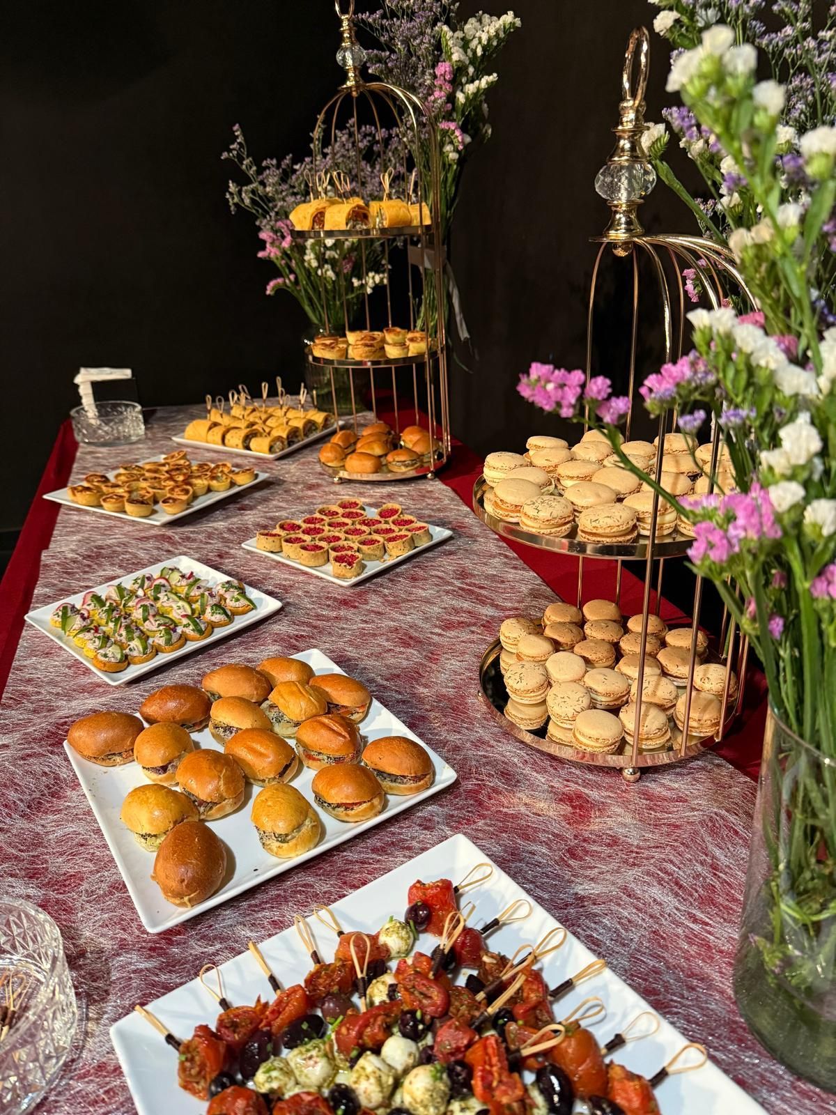 cocktail confidentiel buffet Table de buffet avec diverses pâtisseries et collations, décorée de fleurs, installée à l'extérieur.