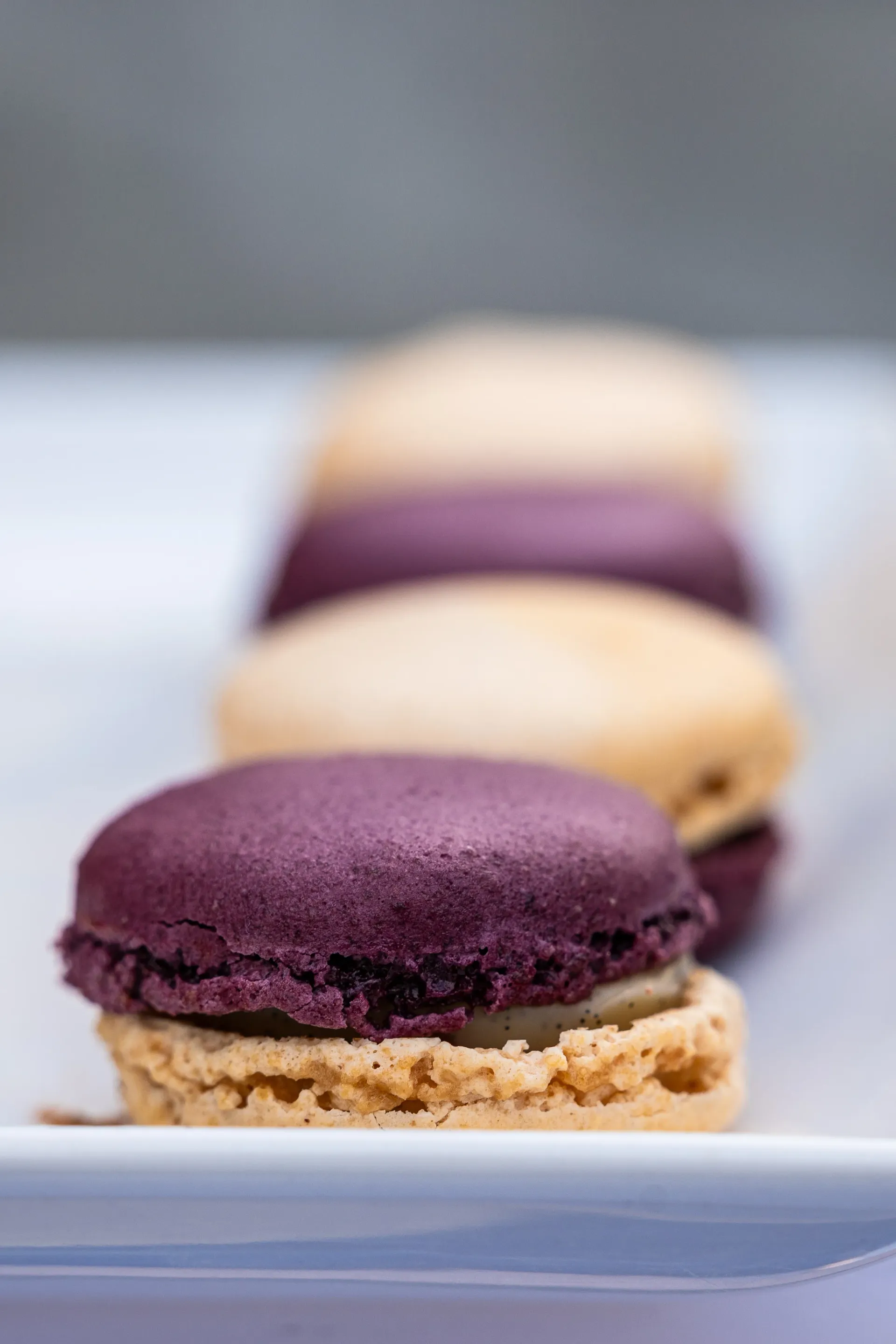 Trois macarons empilés sur une assiette blanche, avec un macaron violet au premier plan.