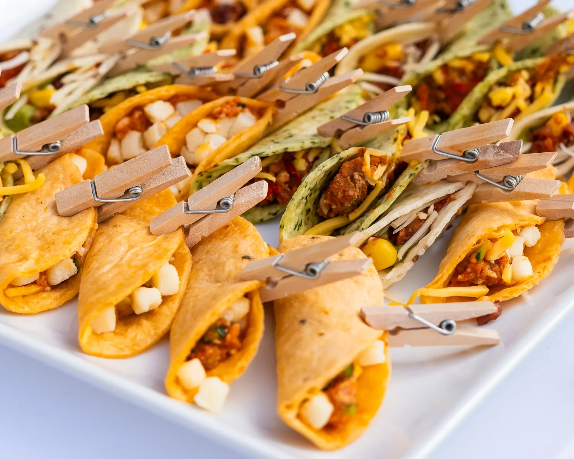 Plateau de mini-tacos apéritifs fourrés à l'orange et présentés sur des cure-dents, sur une assiette blanche