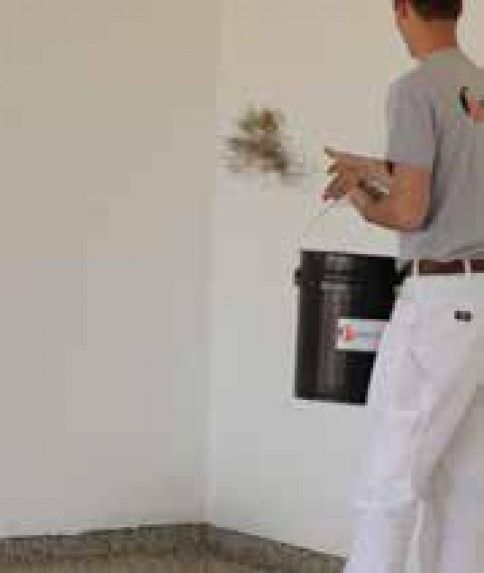 A man is painting a wall with a bucket of paint.