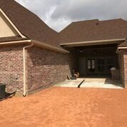 A brick house with a brown roof and a driveway leading to it.