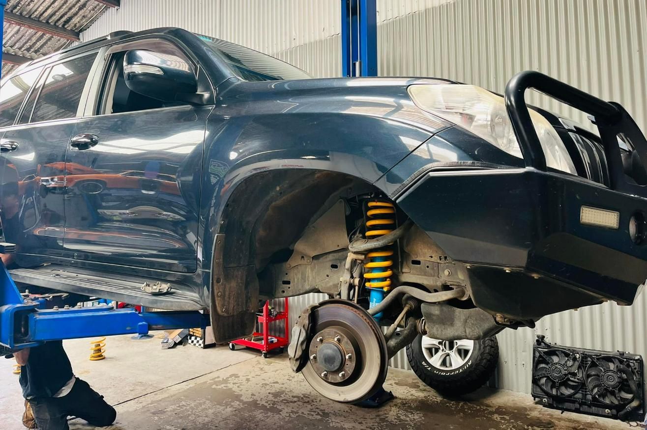 Car lifted in auto shop with front wheel removed, exposing suspension and brake assembly — Mechanic in Wollongong, NSW