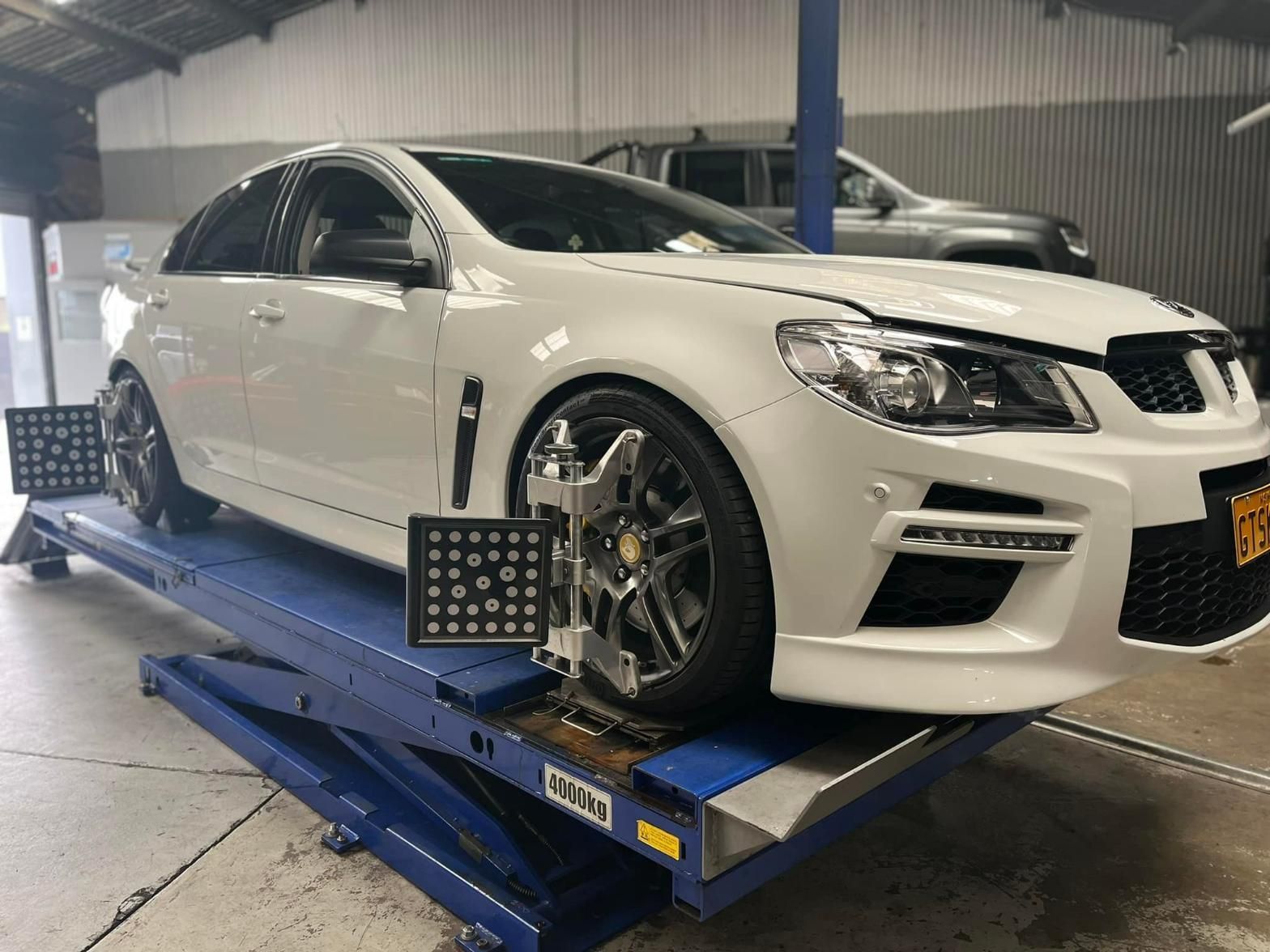 White Car On A Lift For A Wheel Alignment — Wheel Alignment in Wollongong, NSW