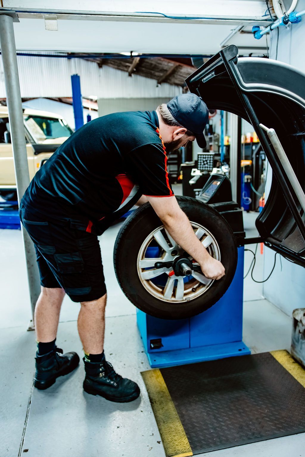 Mechanic inspecting a car wheel on a blue tire balancing machine in an auto shop — Vehicle Inspections in Wollongong, NSW