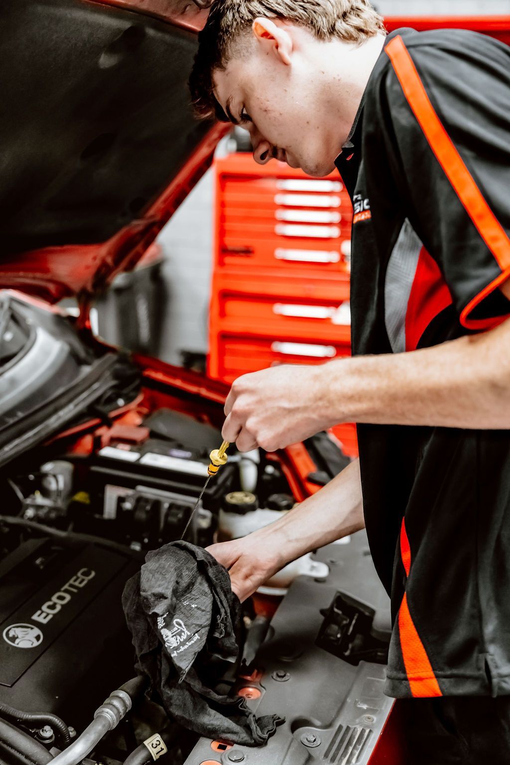 Mechanic inspecting a car engine in a garage, with the hood open and red tool drawers in the background — Vehicle Inspections in Wollongong, NSW