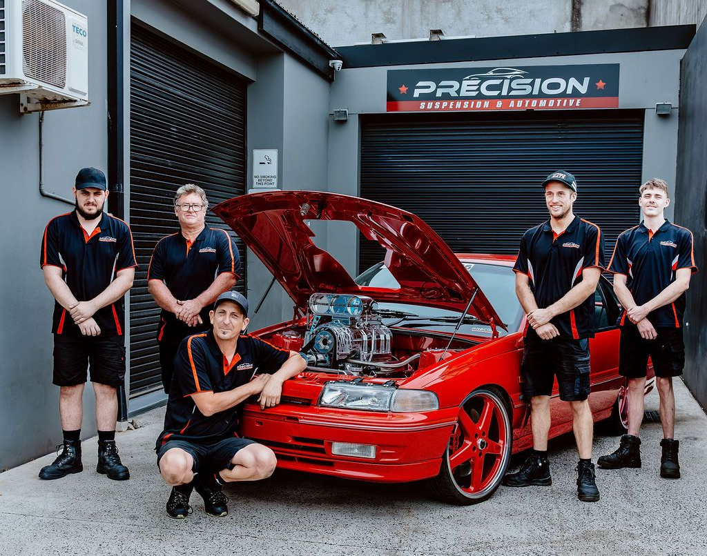 Five people posing with a red sports car outside a tuning shop, hood open — Vehicle Inspections in Wollongong, NSW