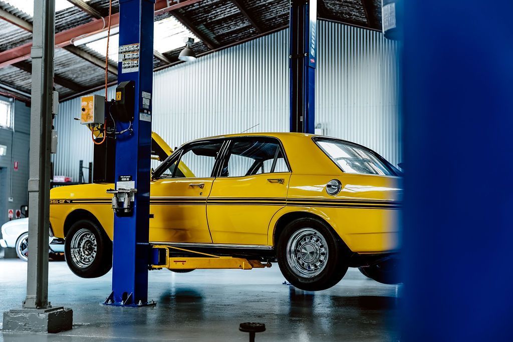 Yellow classic car in an auto repair shop, lifted on a hydraulic rack — Mechanic in Wollongong, NSW