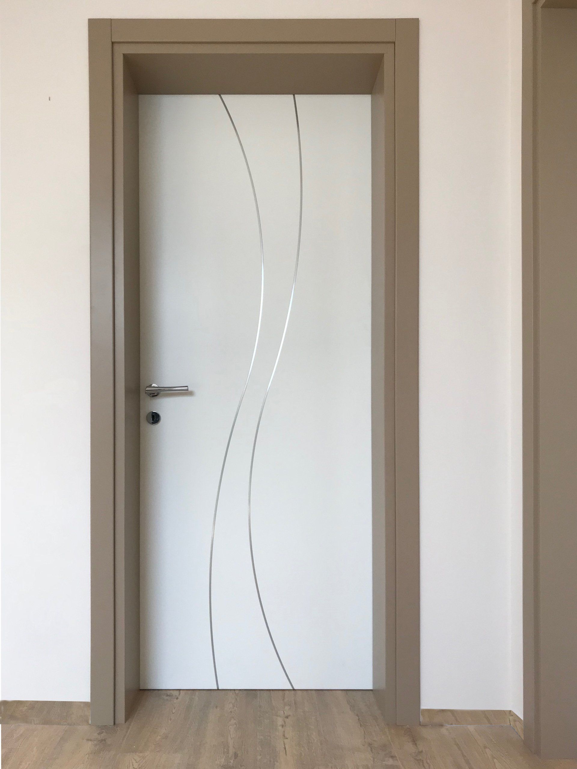Porta interna bianca con due inserti verticali ondulati color argento, incastonati in un telaio marrone chiaro su una parete bianca.