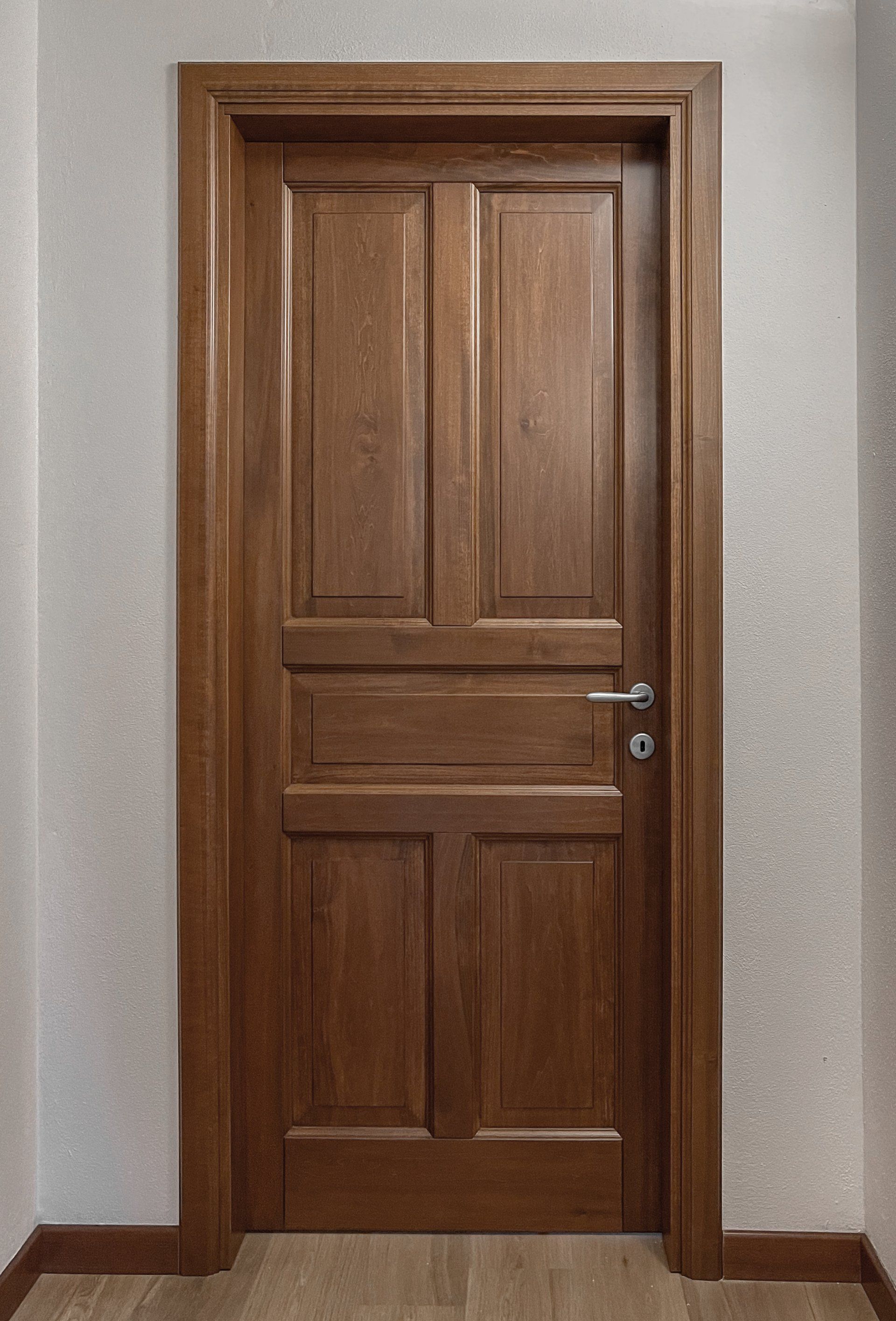 Una porta chiusa in legno marrone con sei pannelli e maniglia a leva argentata, su uno sfondo di pareti bianche.