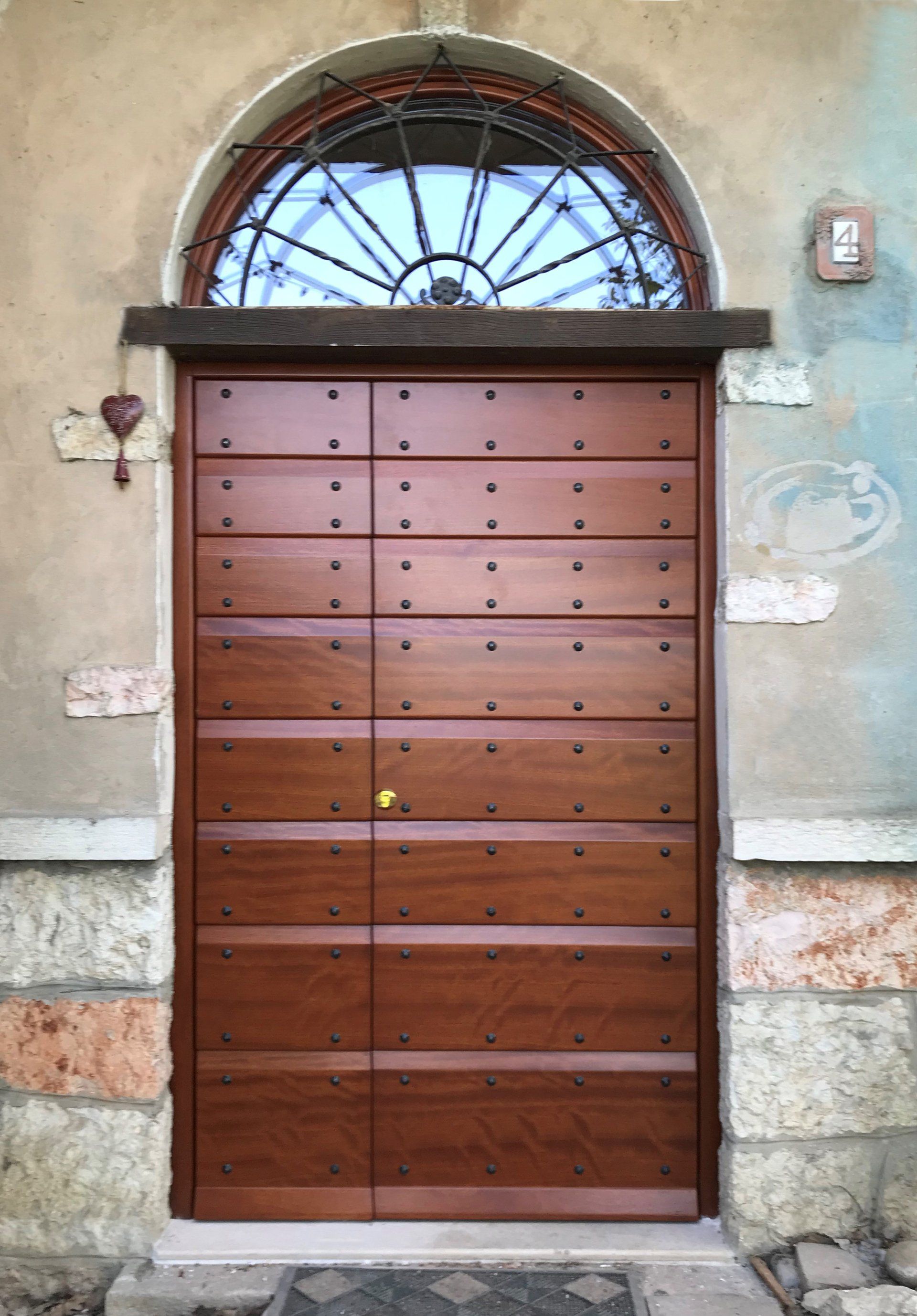 Una doppia porta in legno marrone con borchie sotto una finestra ad arco sulla facciata di un edificio in pietra.