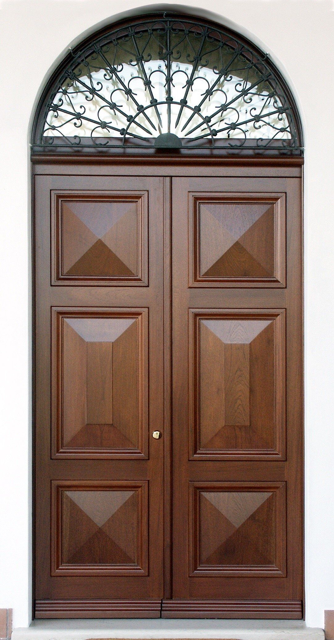 Doppie porte in legno con tre pannelli quadrati in rilievo ciascuna, sormontate da una finestra semicircolare con una grata in ferro battuto decorata.