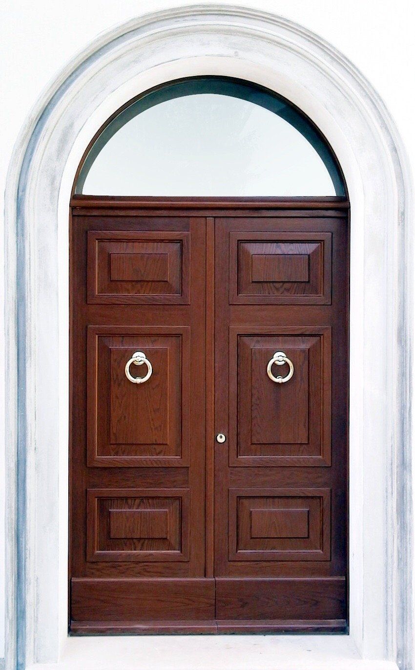 Una porta a due ante in legno scuro con due battenti rotondi, incastonata in una cornice ad arco bianca.