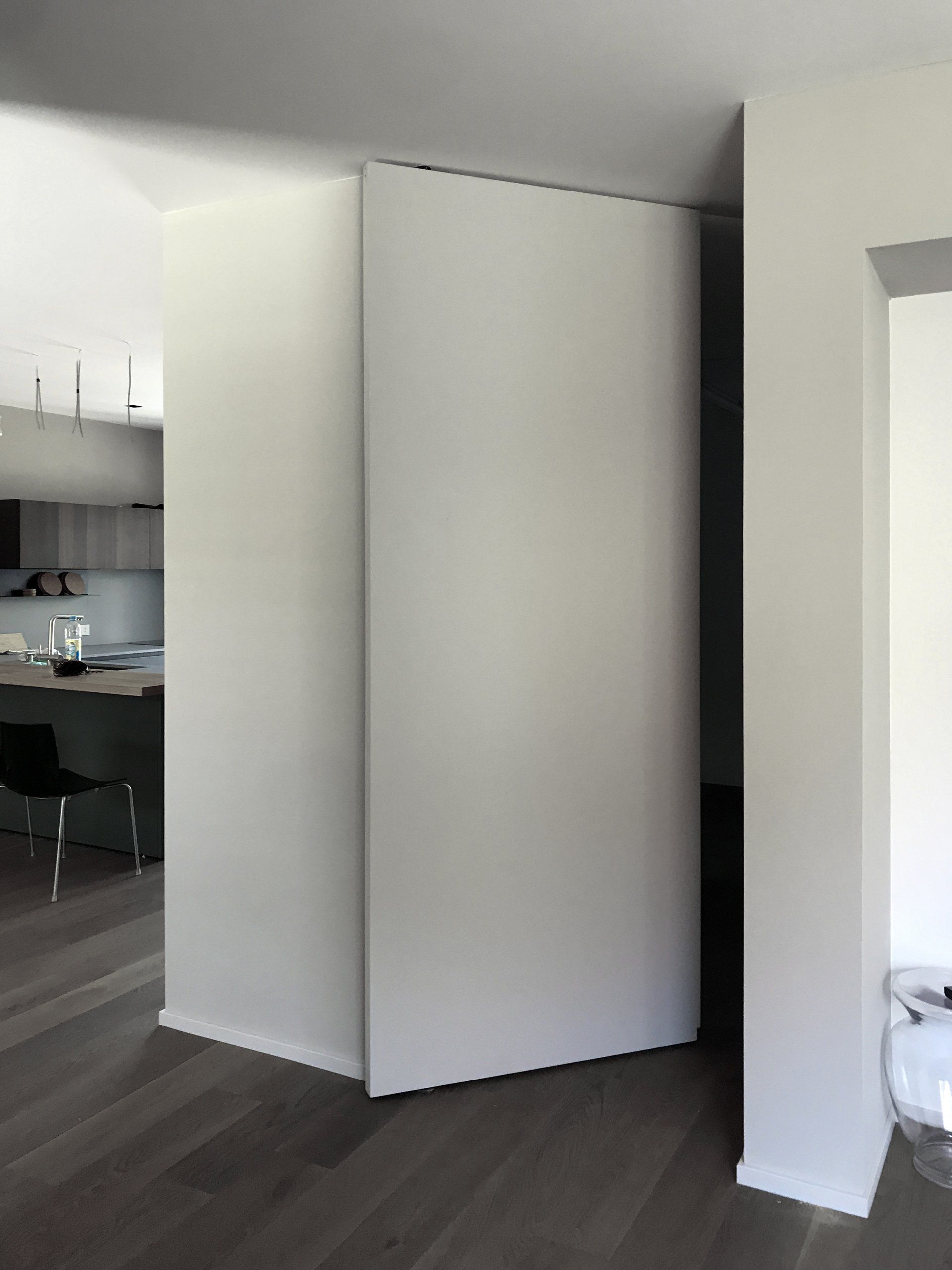 Una porta interna bianca, senza giunture e a filo muro, leggermente socchiusa, inserita in una casa moderna con pavimento in legno grigio.