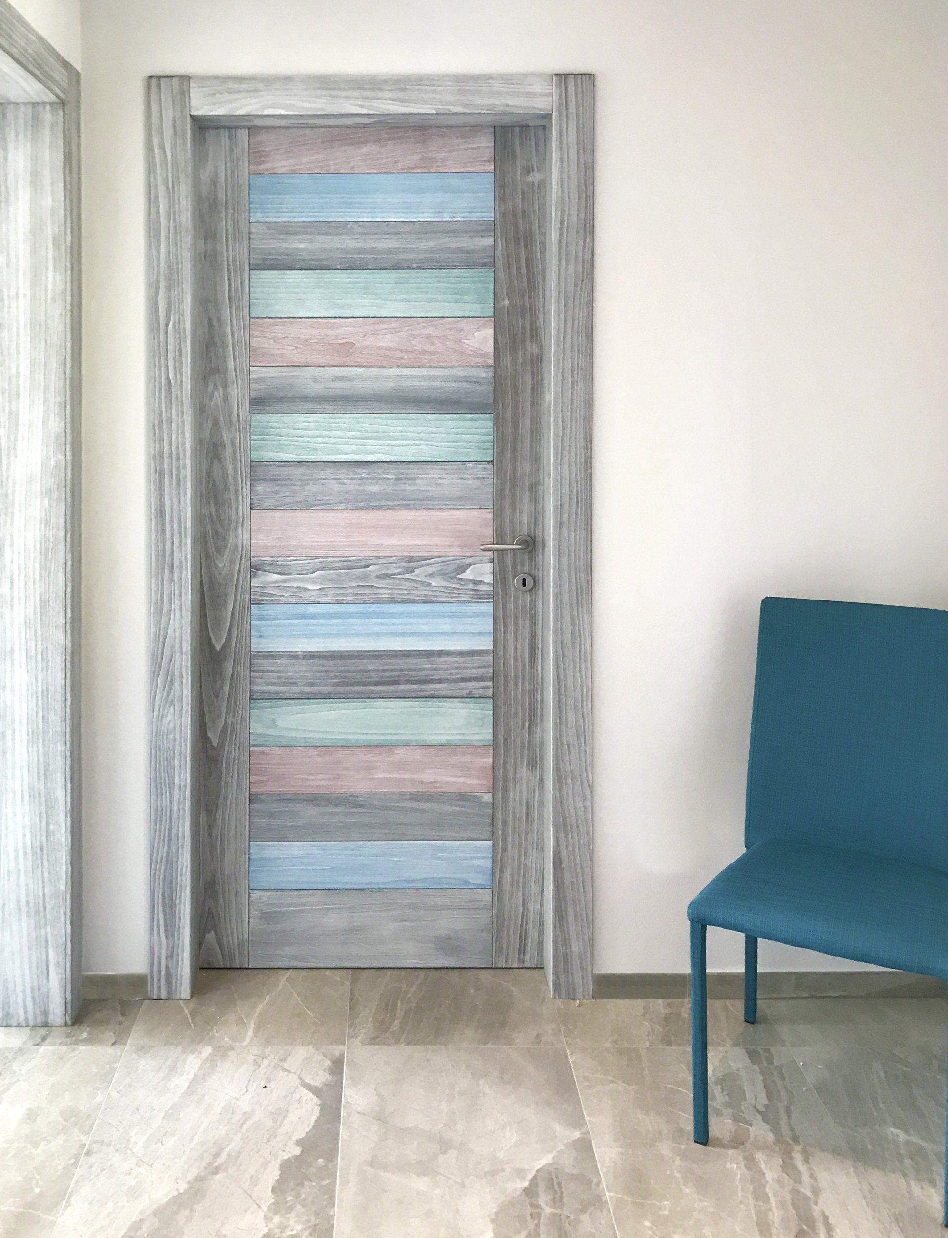 Un interno moderno con una porta in stile rustico caratterizzata da strisce orizzontali nei toni tenui del blu, del rosa e del grigio, accanto a una sedia blu.