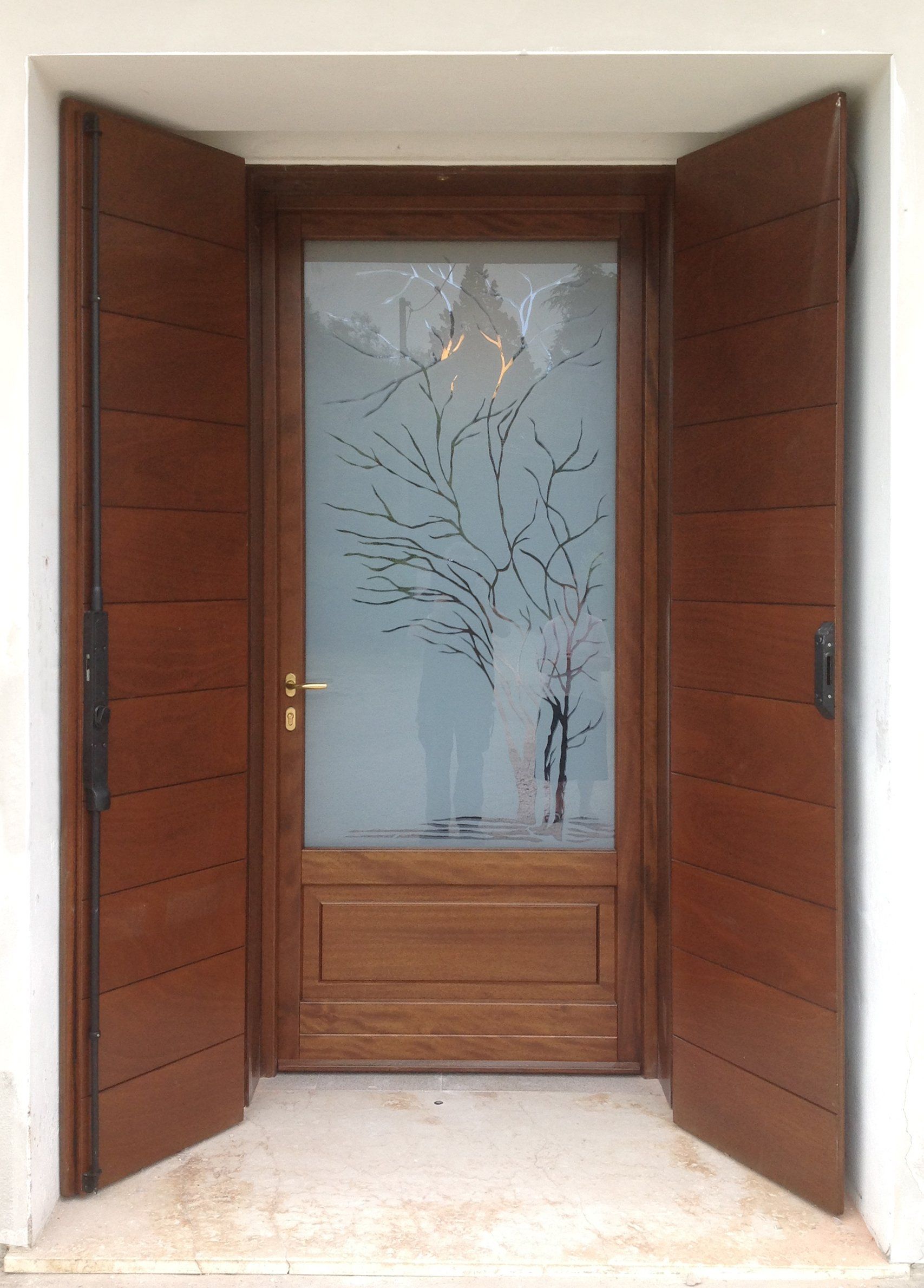 Una porta d'ingresso in legno con un pannello in vetro satinato decorato con un motivo ad albero, incorniciata da persiane in legno a giorno abbinate.