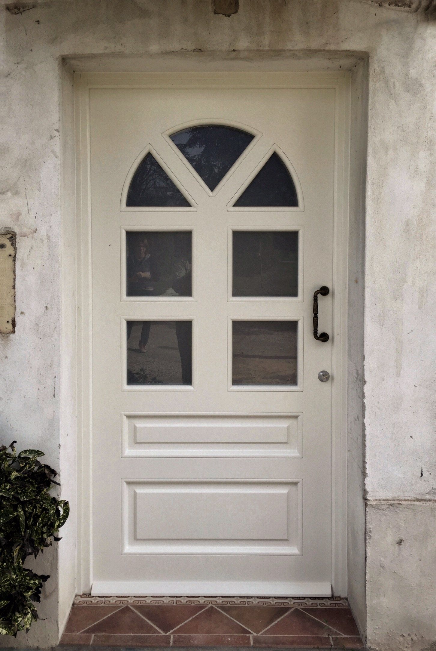 Una porta in legno color crema con pannelli in vetro e parte superiore ad arco, incastonata in un muro di pietra lavorata.