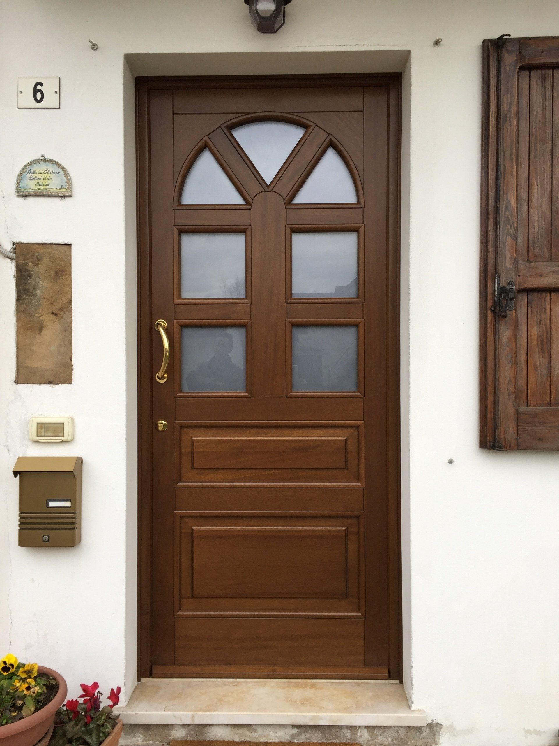 Una porta d'ingresso in legno scuro con pannelli di vetro nella parte superiore, una maniglia dorata e una cassetta delle lettere a muro accanto.