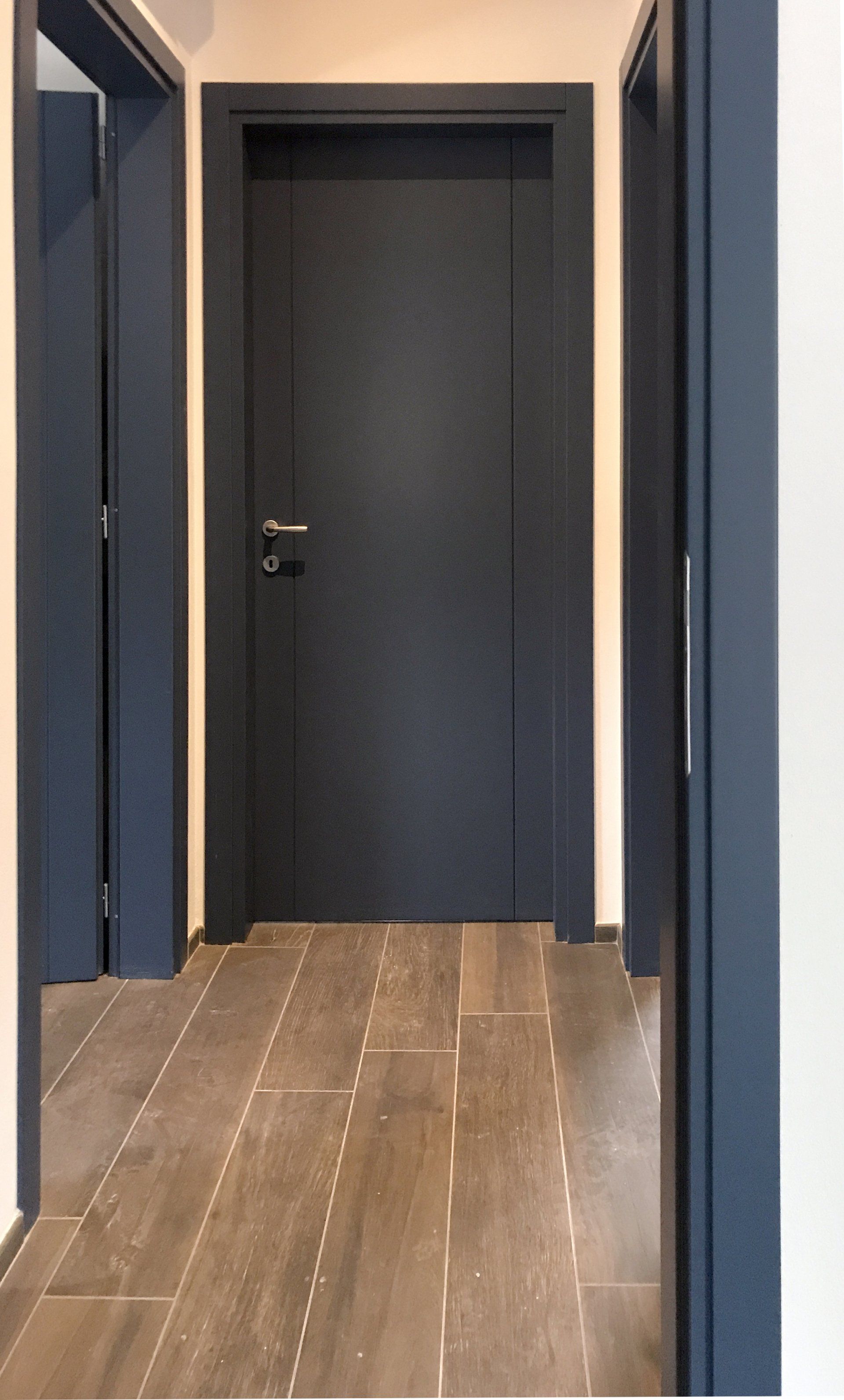 Un corridoio con porte e infissi grigio scuro su un pavimento in legno chiaro.