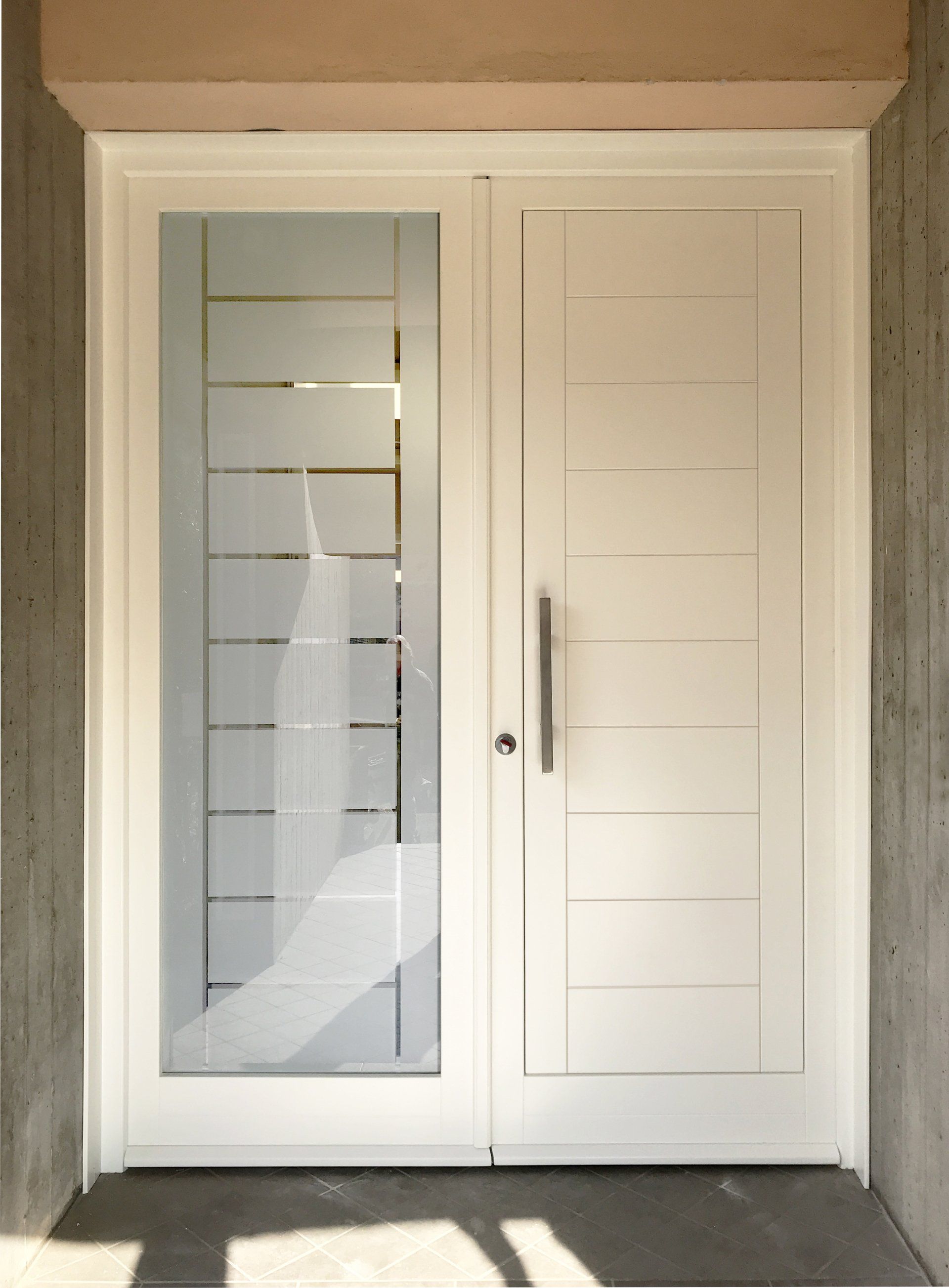 Una porta moderna bianca con pannello verticale in vetro satinato caratterizzato da linee orizzontali incise e maniglia metallica.