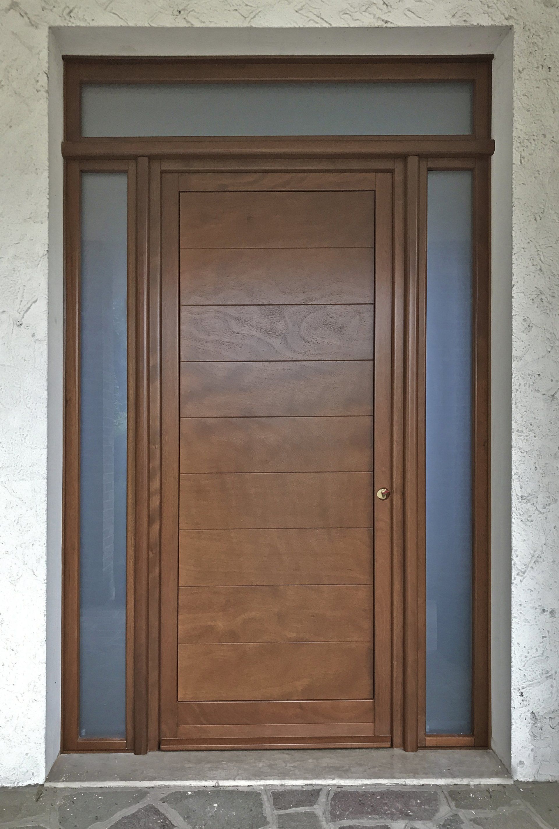 Una moderna porta d'ingresso in legno marrone con pannelli orizzontali, fiancheggiata da due finestre laterali verticali in vetro satinato e da un sopraluce.