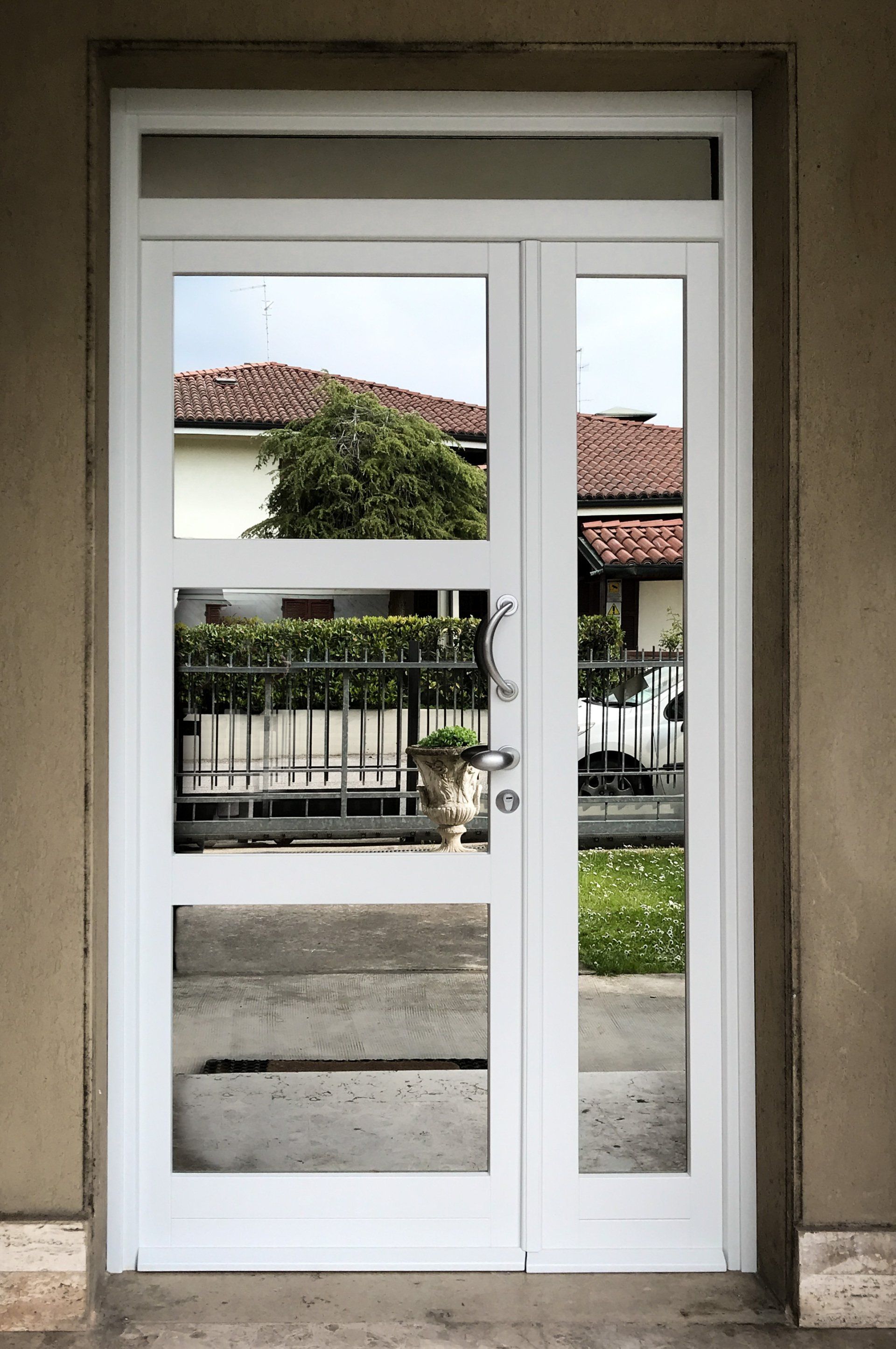 Una porta bianca con pannelli di vetro incastonata in una parete liscia, che riflette la casa e il giardino circostanti.