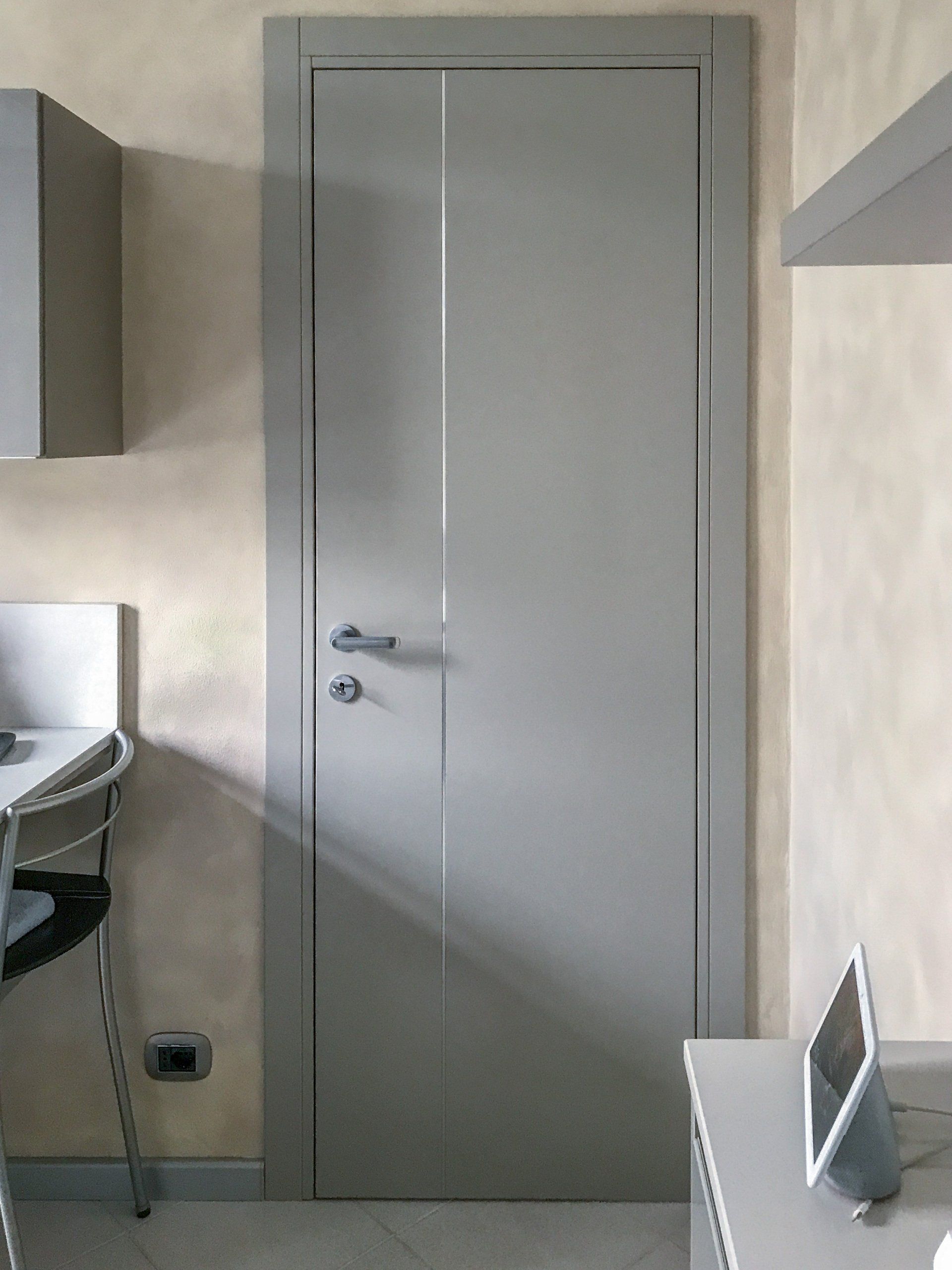 Una moderna porta interna grigio chiaro con un dettaglio a scanalatura verticale, installata in una stanza con pareti beige texturizzate.