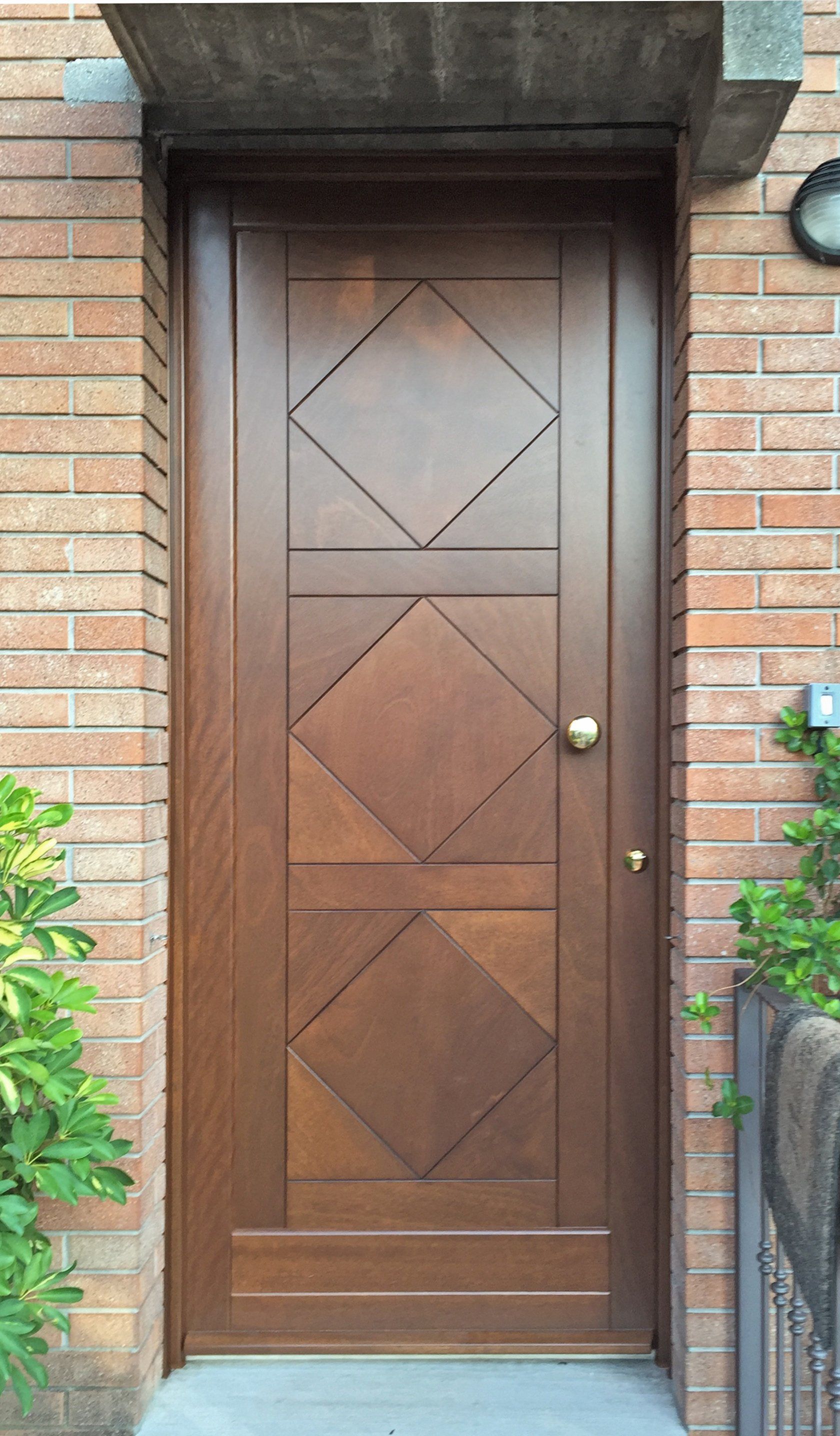 Una porta di legno marrone con pannelli a forma di diamante in un ingresso in mattoni.