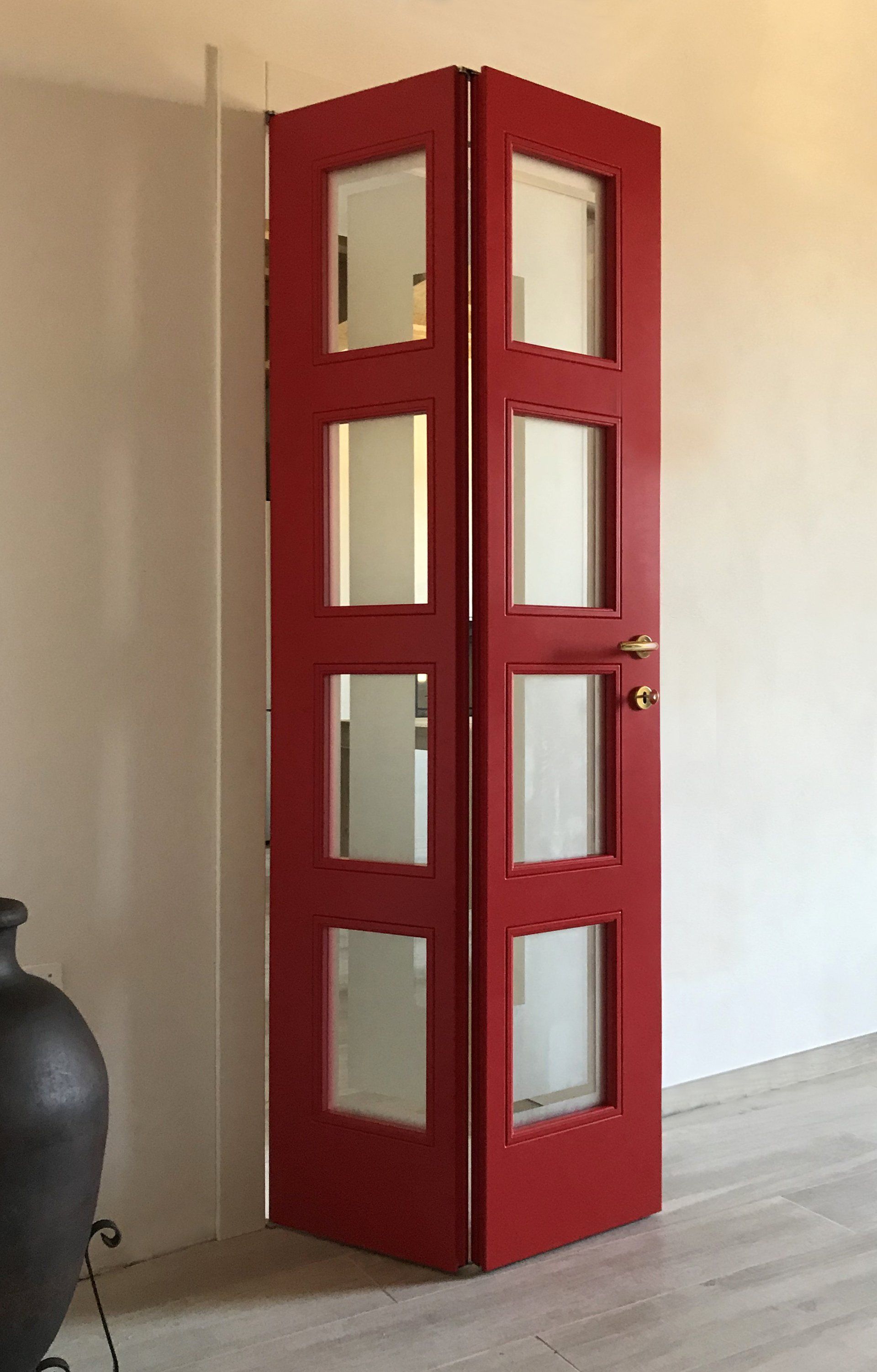 Una porta a soffietto rossa con quattro pannelli rettangolari in vetro satinato in ogni sezione, posizionata in un angolo di una stanza.