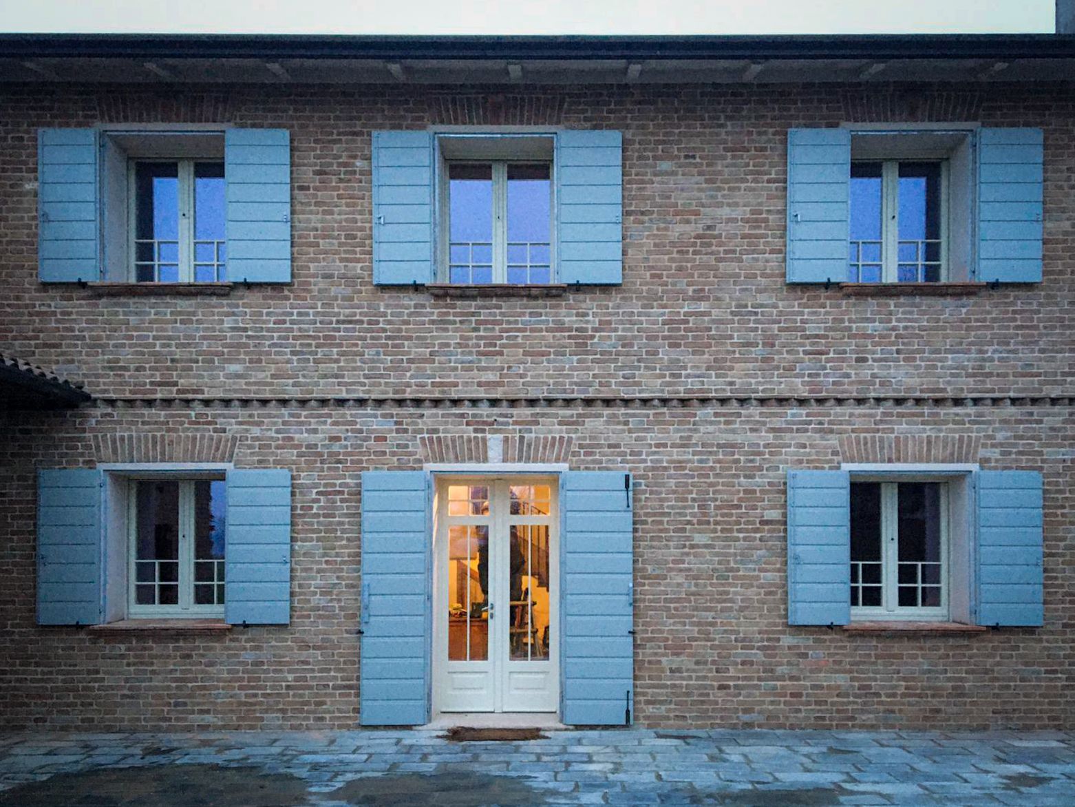 Una casa a due piani in mattoni con una porta centrale in vetro e persiane azzurre su tutte le finestre.