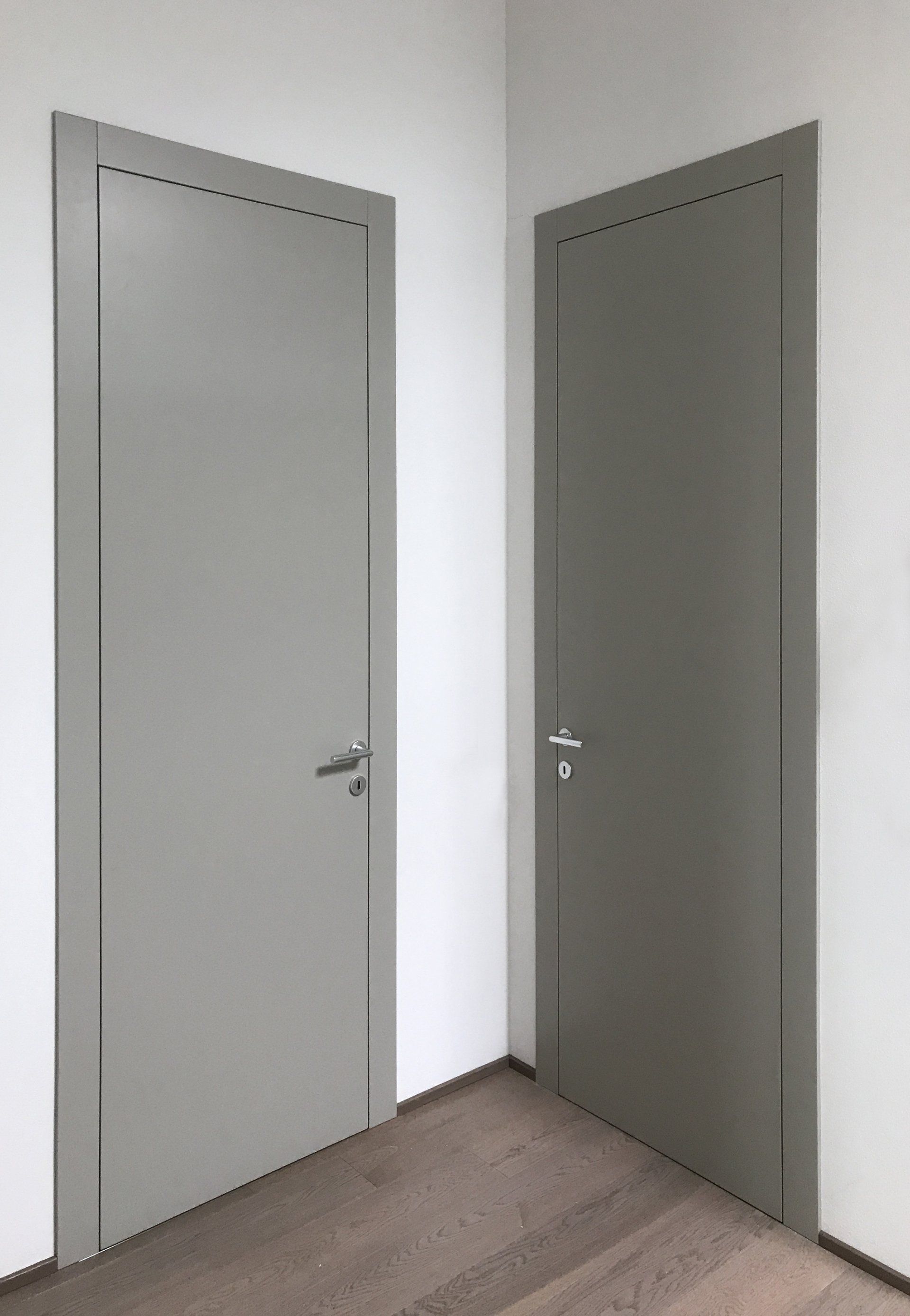 Due porte grigie con fessure di ventilazione nella parte superiore, incastonate in pareti bianche sopra un pavimento in legno.