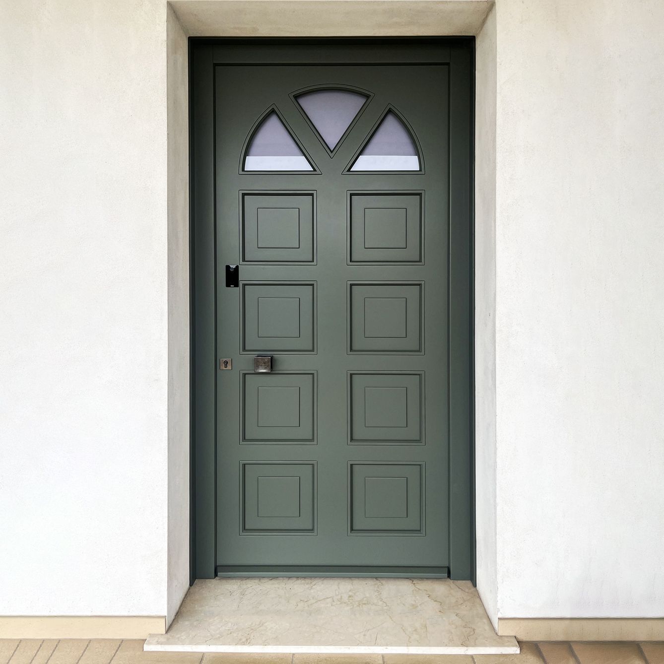 Una porta d'ingresso ad arco in legno marrone chiaro con pannelli in vetro e un disegno circolare, fiancheggiata da due pilastri in mattoni con lampade.