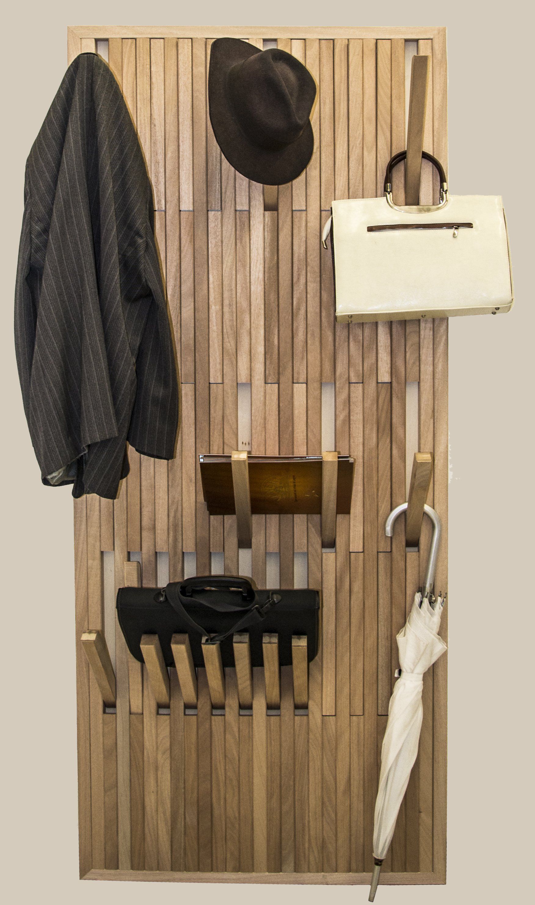Un appendiabiti verticale a doghe di legno che regge un cappello, una borsa, un ombrello, un cappotto scuro e vestiti piegati.