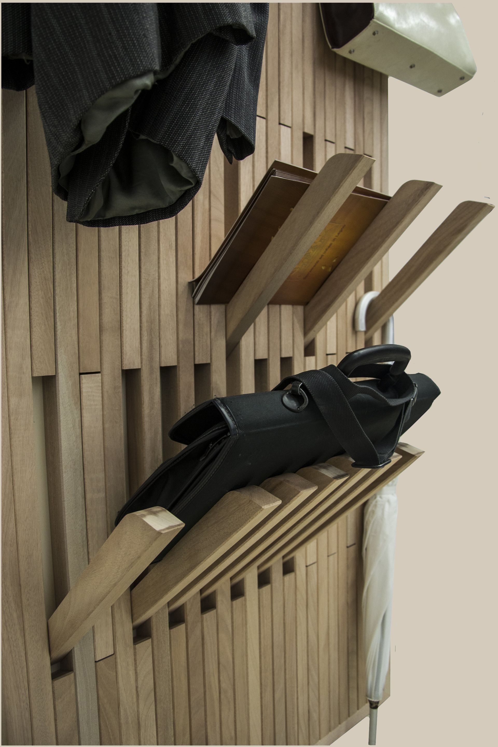 Un organizer da parete a doghe di legno con ripiani modulari per riporre cappotti, borse e ombrelli.
