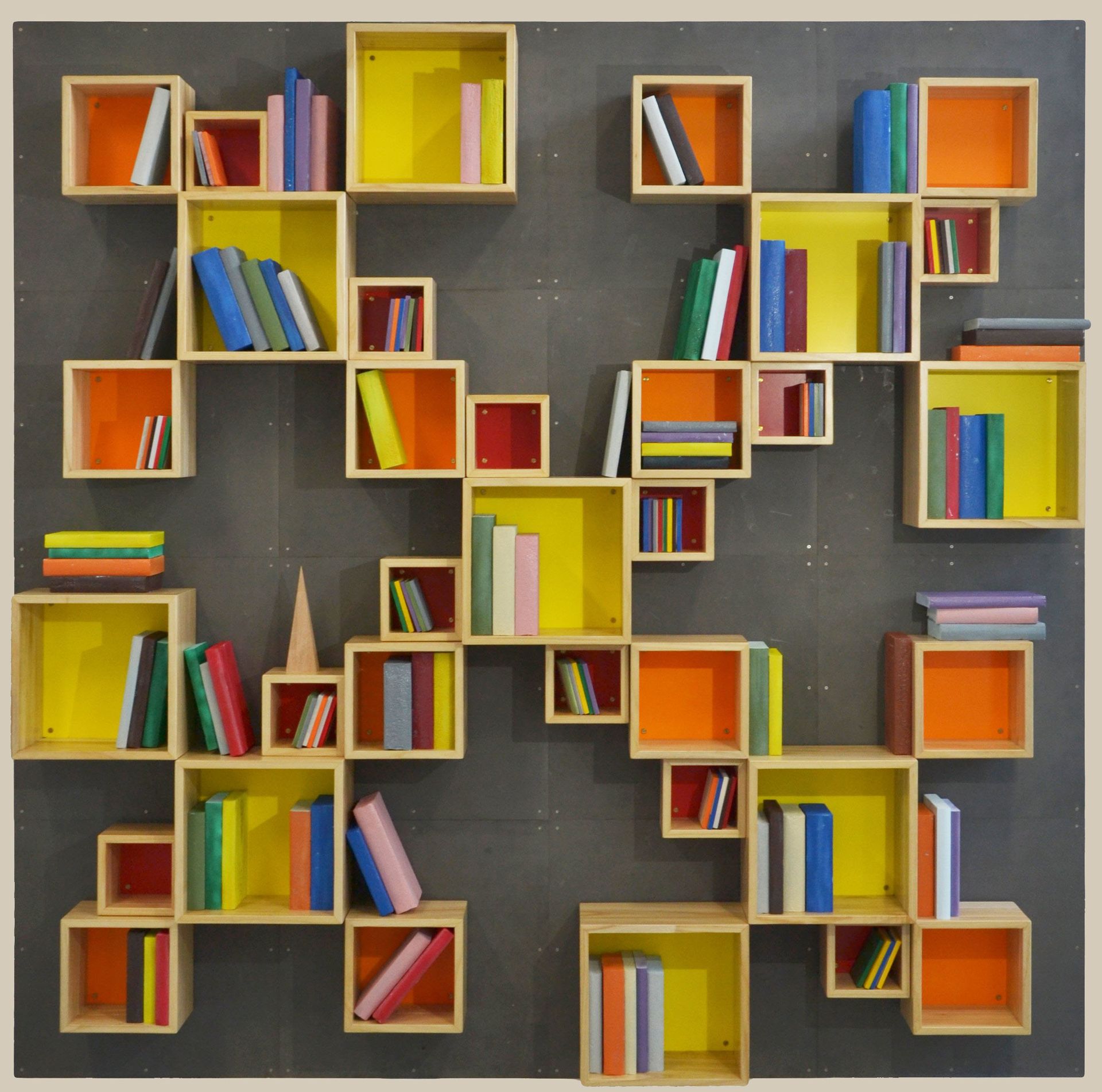 Un sistema di mensole modulari a parete con retro giallo e arancione, riempito con vari libri colorati su una parete scura.