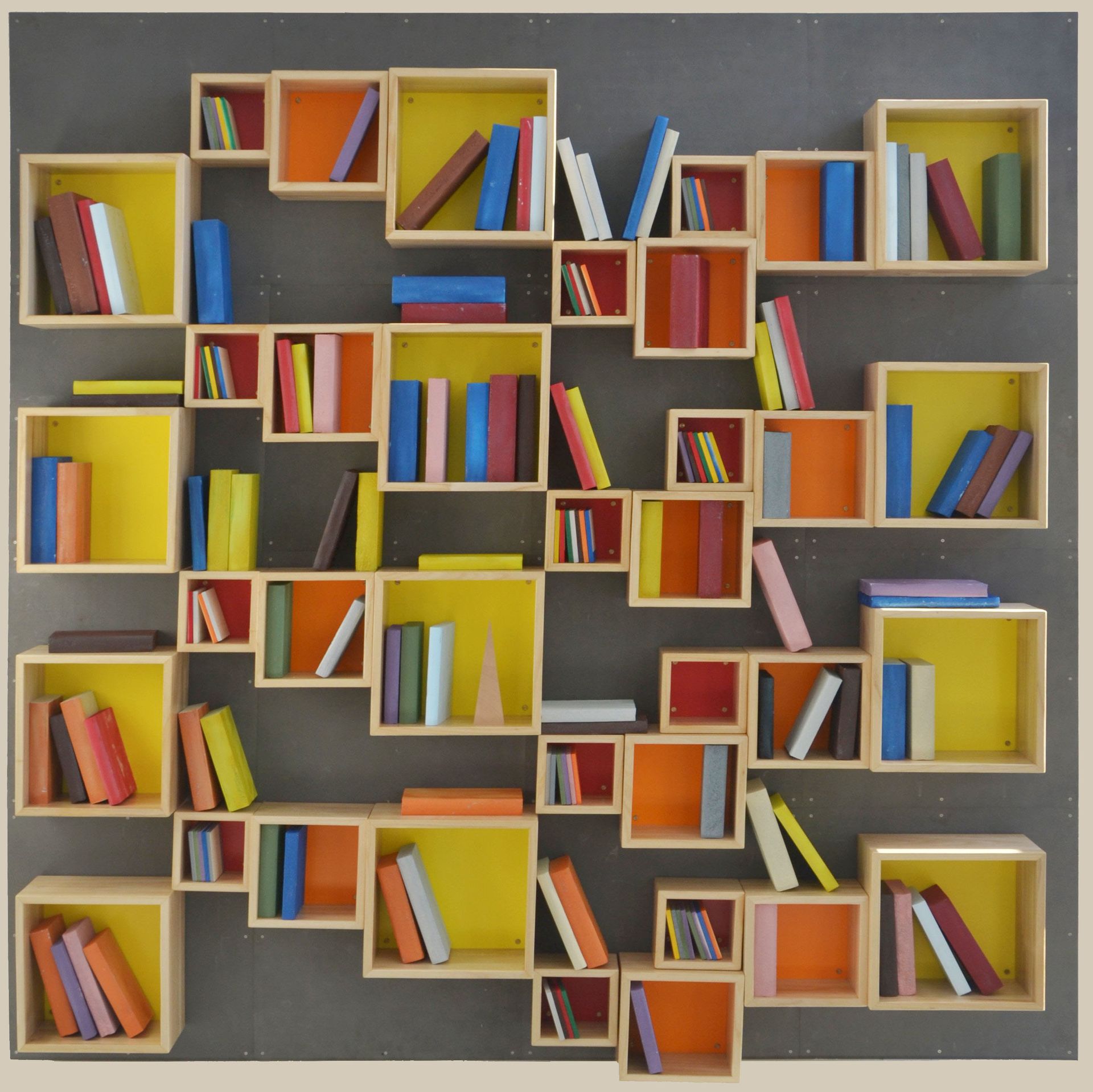 Una composizione a parete di mensole in legno irregolari, a forma di scatola, con retro giallo e arancione, piene di libri colorati.