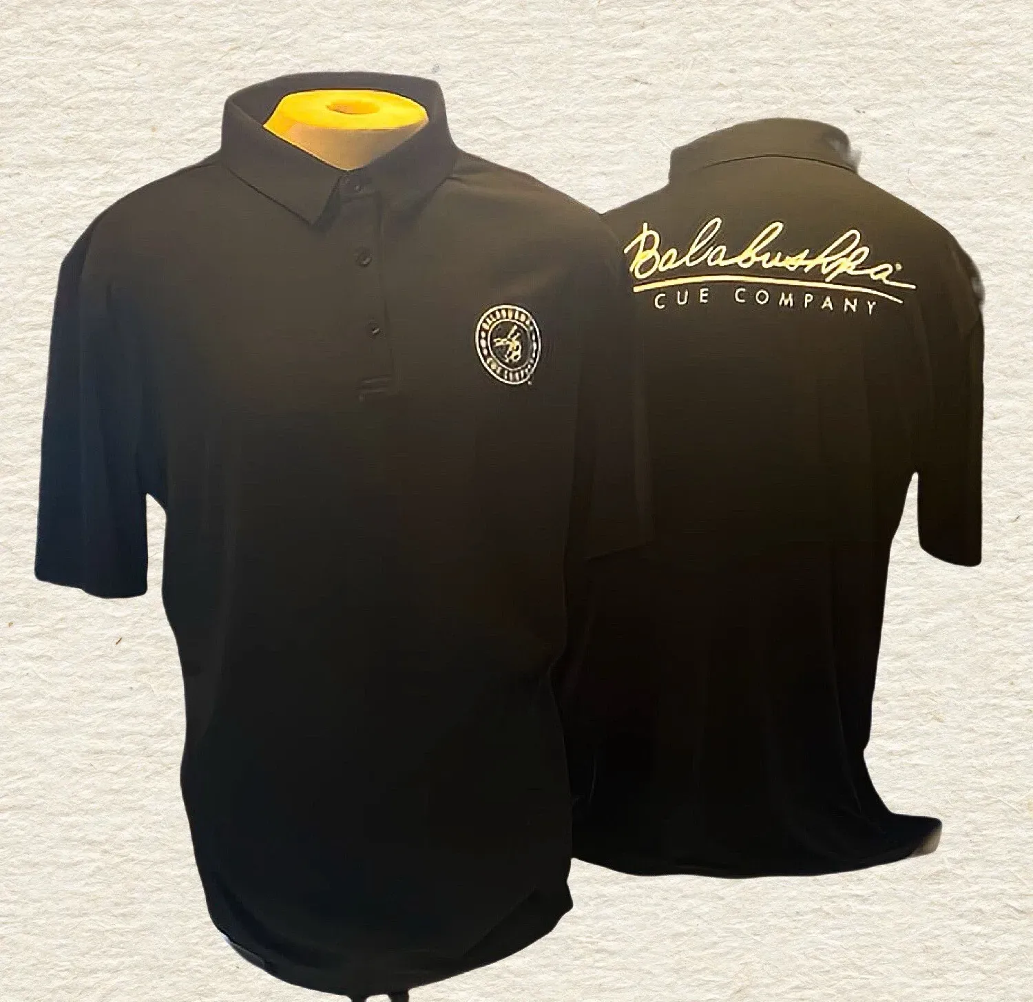 Black polo shirt shown front and back, with white embroidered logos on the chest and back.