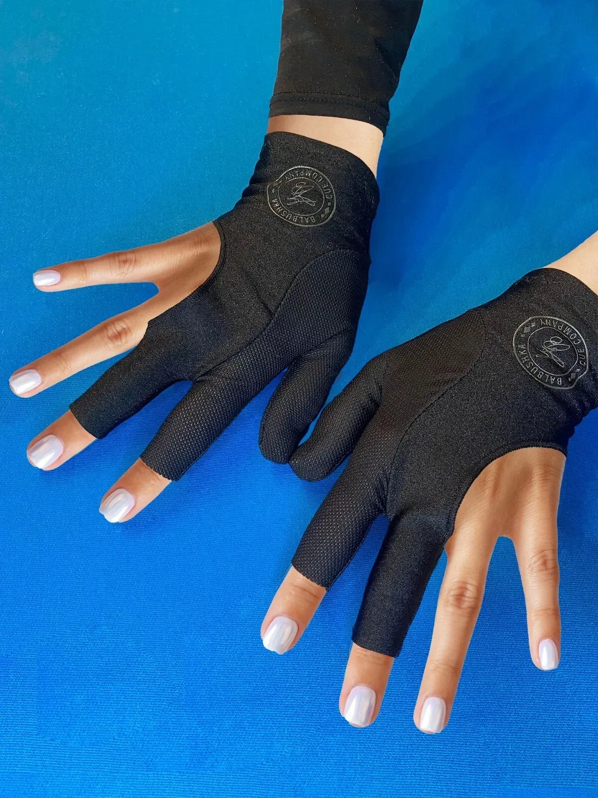 Two hands wearing black fingerless gloves on a blue surface, fingers spread.