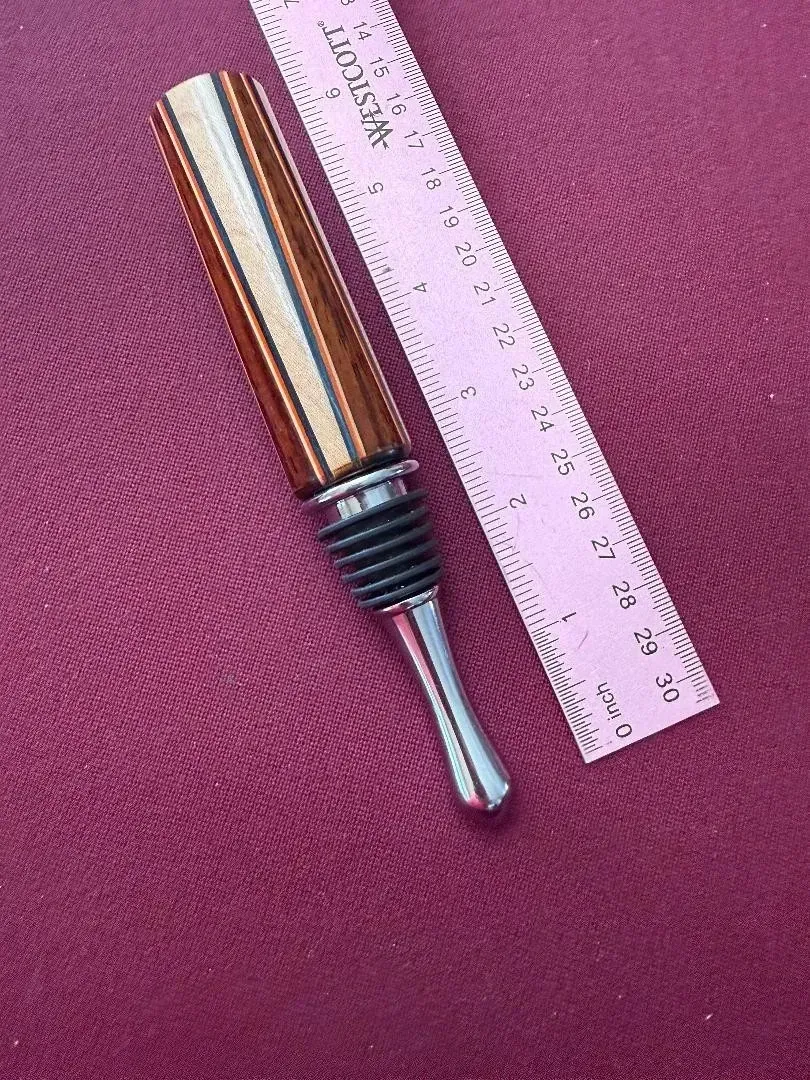 Small metal-handled tool with dual prongs beside a pink ruler on a textured magenta surface