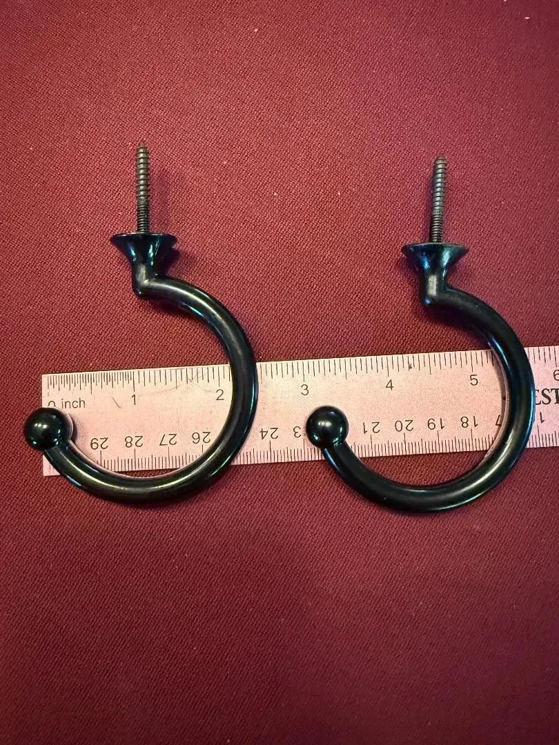 Two black metal hook earrings beside a ruler on a red fabric background