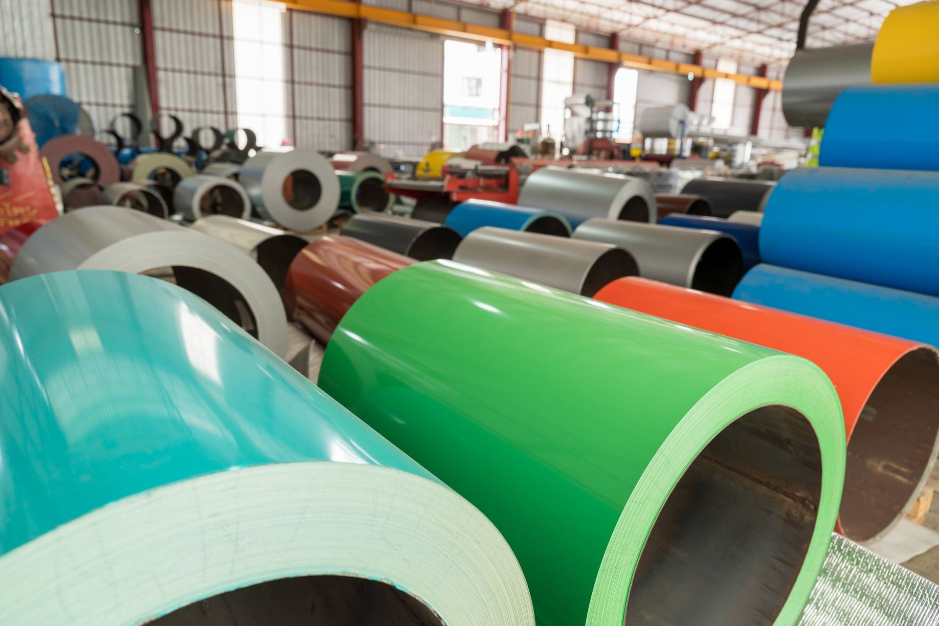 Coils of colorful metal sheets in a warehouse setting.