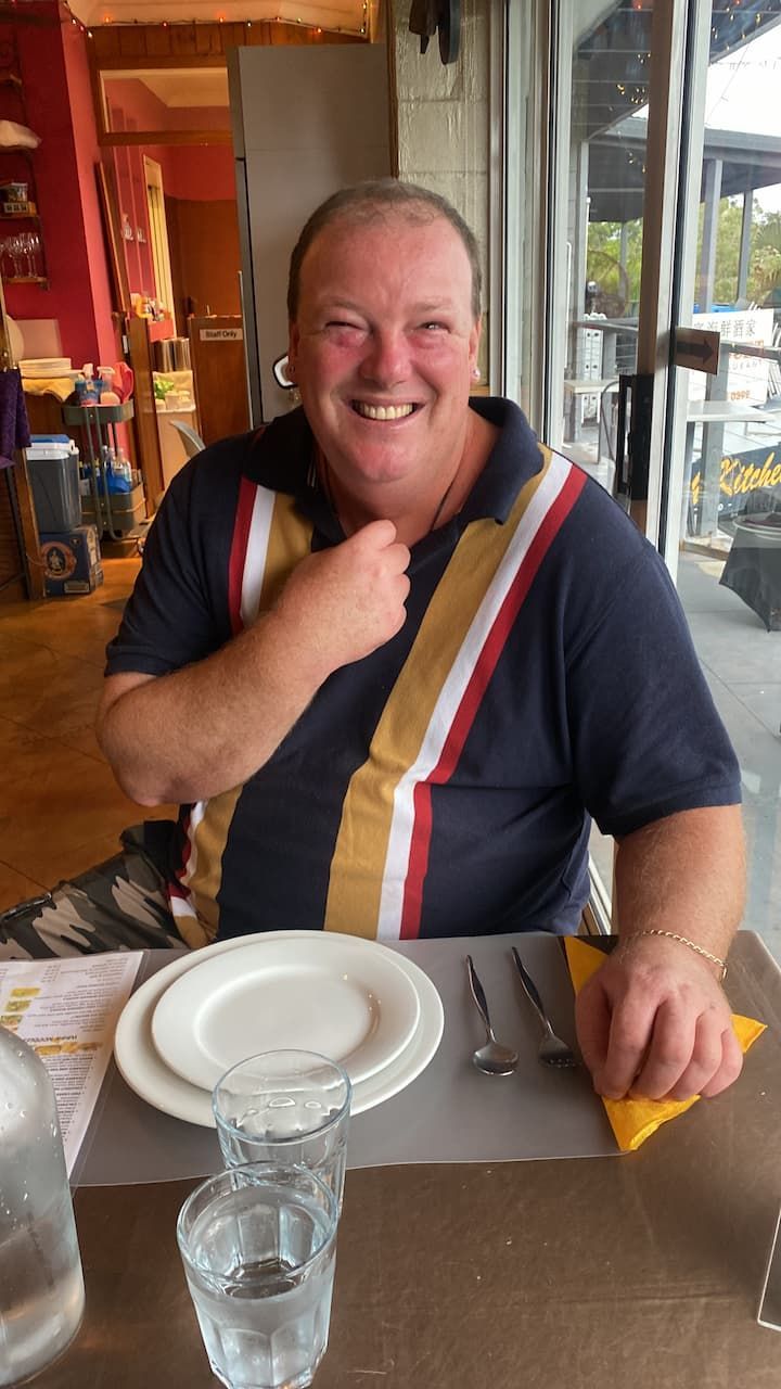 A Man is Smiling While Sitting at a Table With Plates and Glasses — Mentally Hooked in Helensvale, QLD