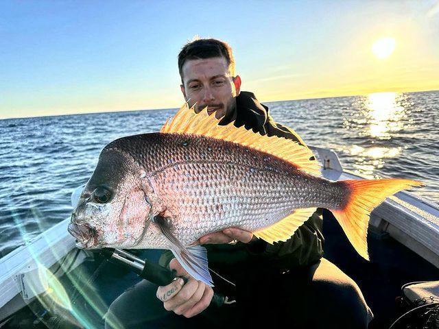 A Man is Holding a Large Fish on a Boat in the Ocean — Mentally Hooked in Helensvale, QLD