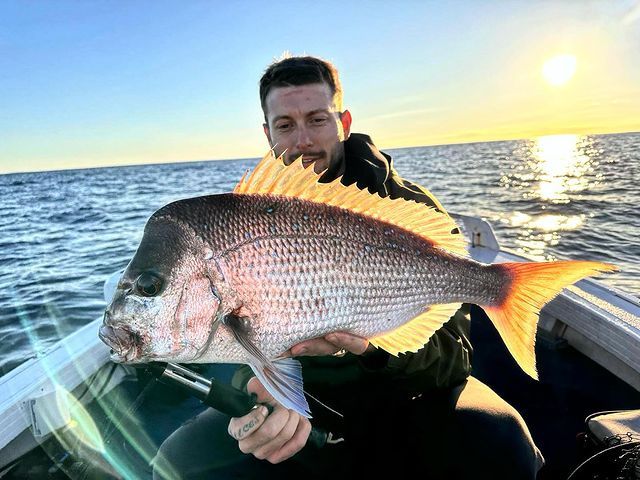 A Man is Sitting on a Boat Holding a Large Fish — Mentally Hooked in Helensvale, QLD