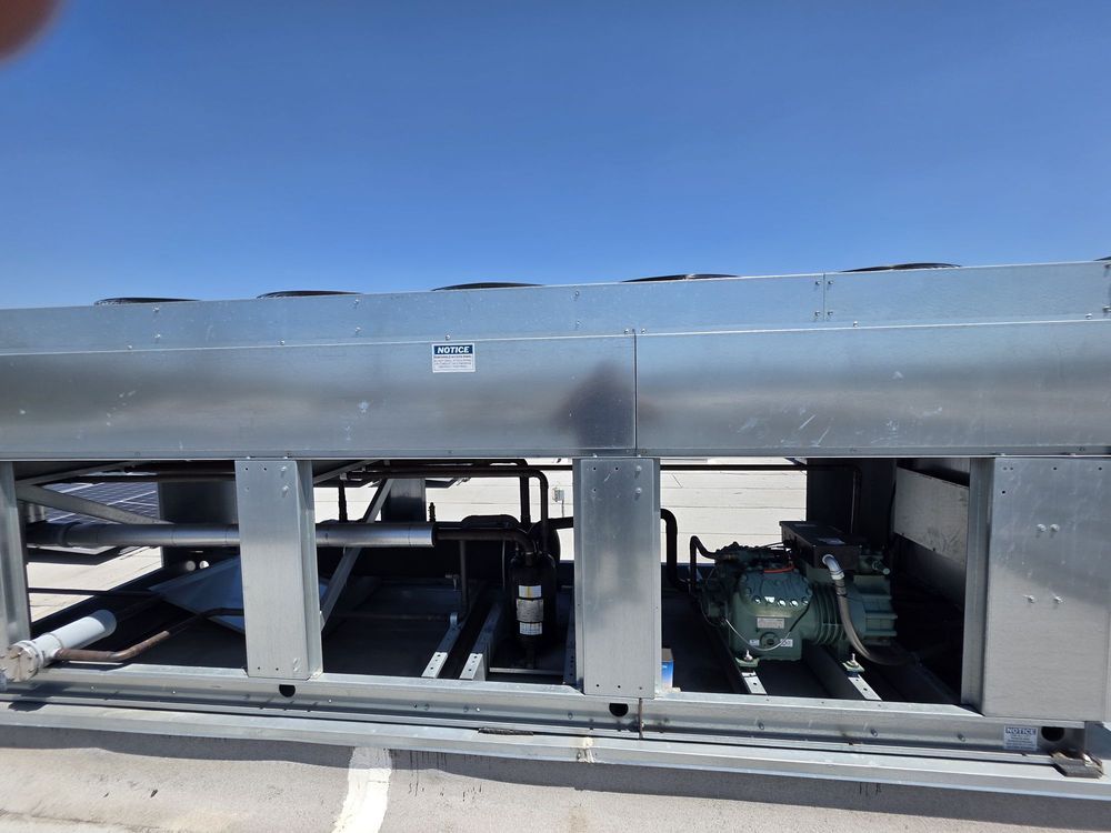 Damaged gray rooftop HVAC unit with open panels against a blue sky